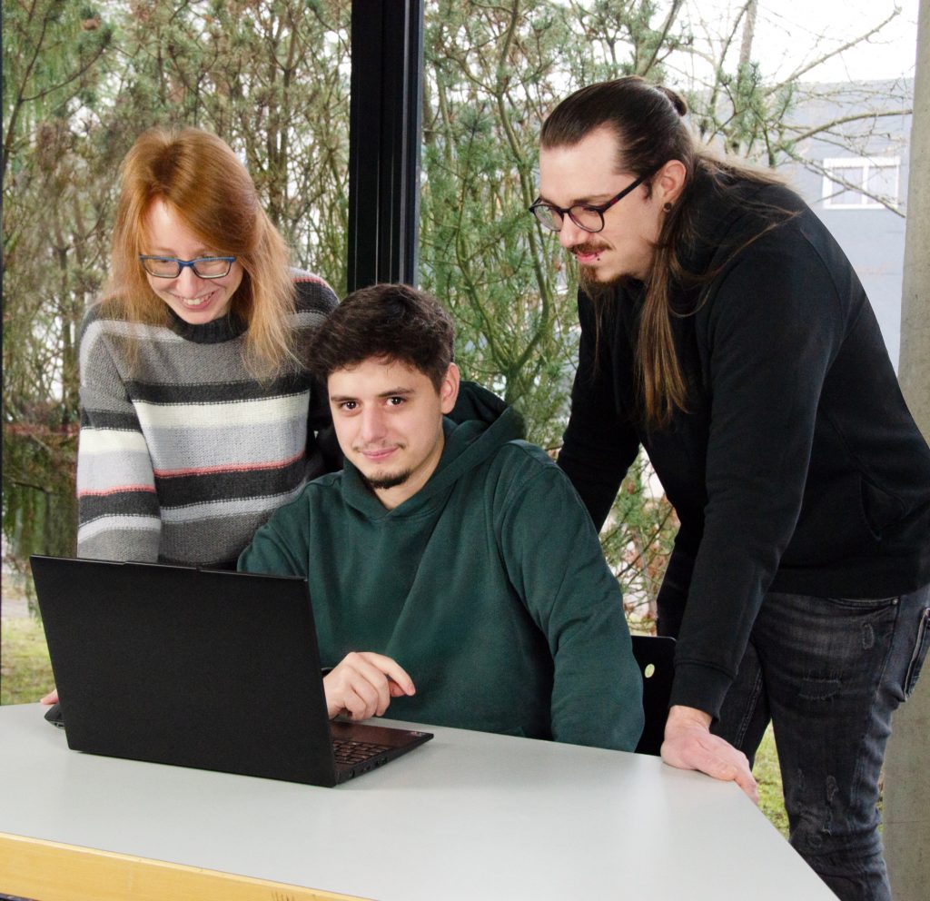 Zwei Azubis stehen mit dem Ausbildungsbetreuer am Laptop