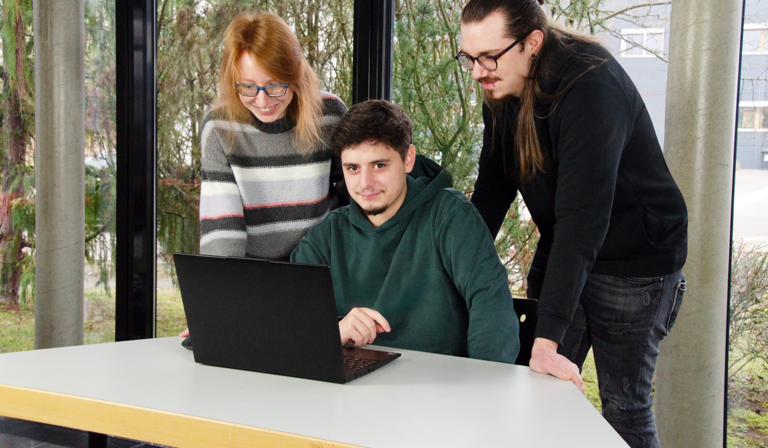 Zwei Azubis stehen mit dem Ausbildungsbetreuer am Laptop